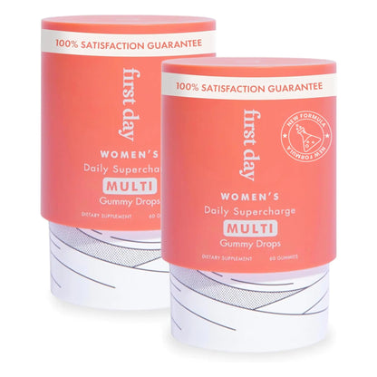 Two cylindrical containers of First Day Women's Daily Supercharge Multi Gummy Drops with red branding and white text, sitting side by side.
